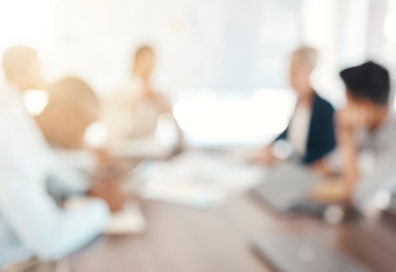 Blurred image of people sitting around a board room table.