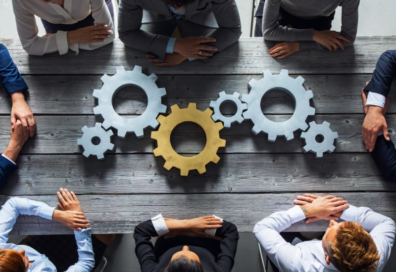 Group of business people joining together silver and golden colored gears on table at workplace