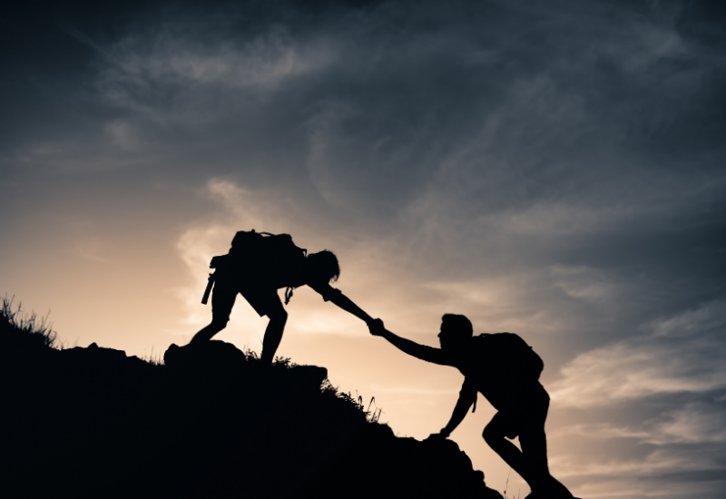 Mountain combiners helping each other climb up a mountain edge.